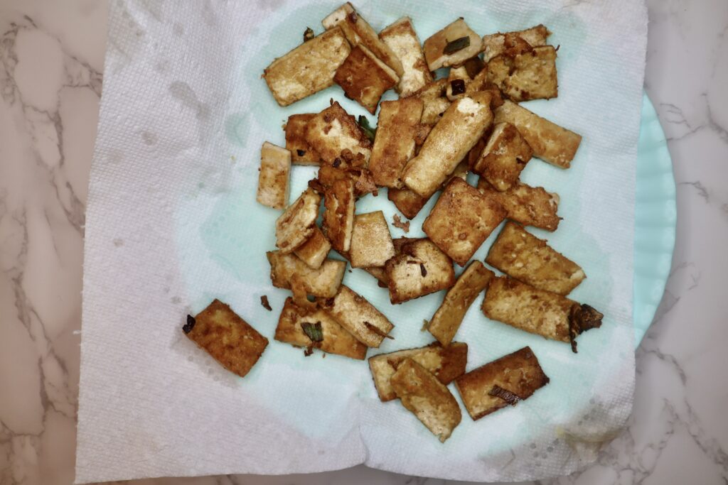 Fried tofu drying on paper towel lined plate