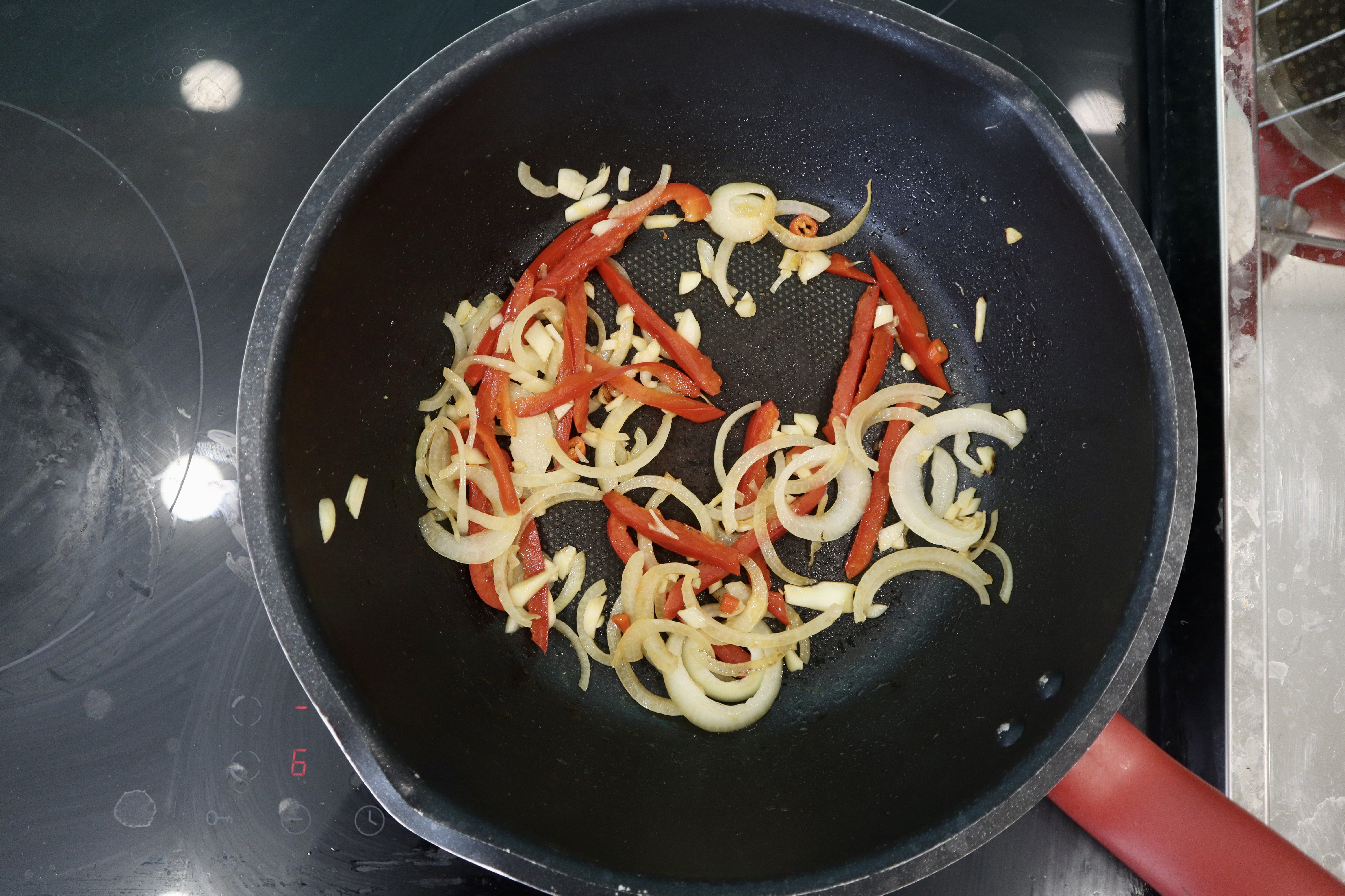 Sautéed onion, garlic, chilli, and red pell pepper in a pan