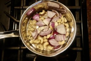red onion, cashews, and garlic cloves in a pot of water