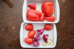 Red pepper, onion, garlic, and tomatoes on a baking sheet