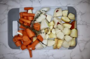chopped carrots, potatoes, onion, thyme, garlic, and ginger on a cutting board