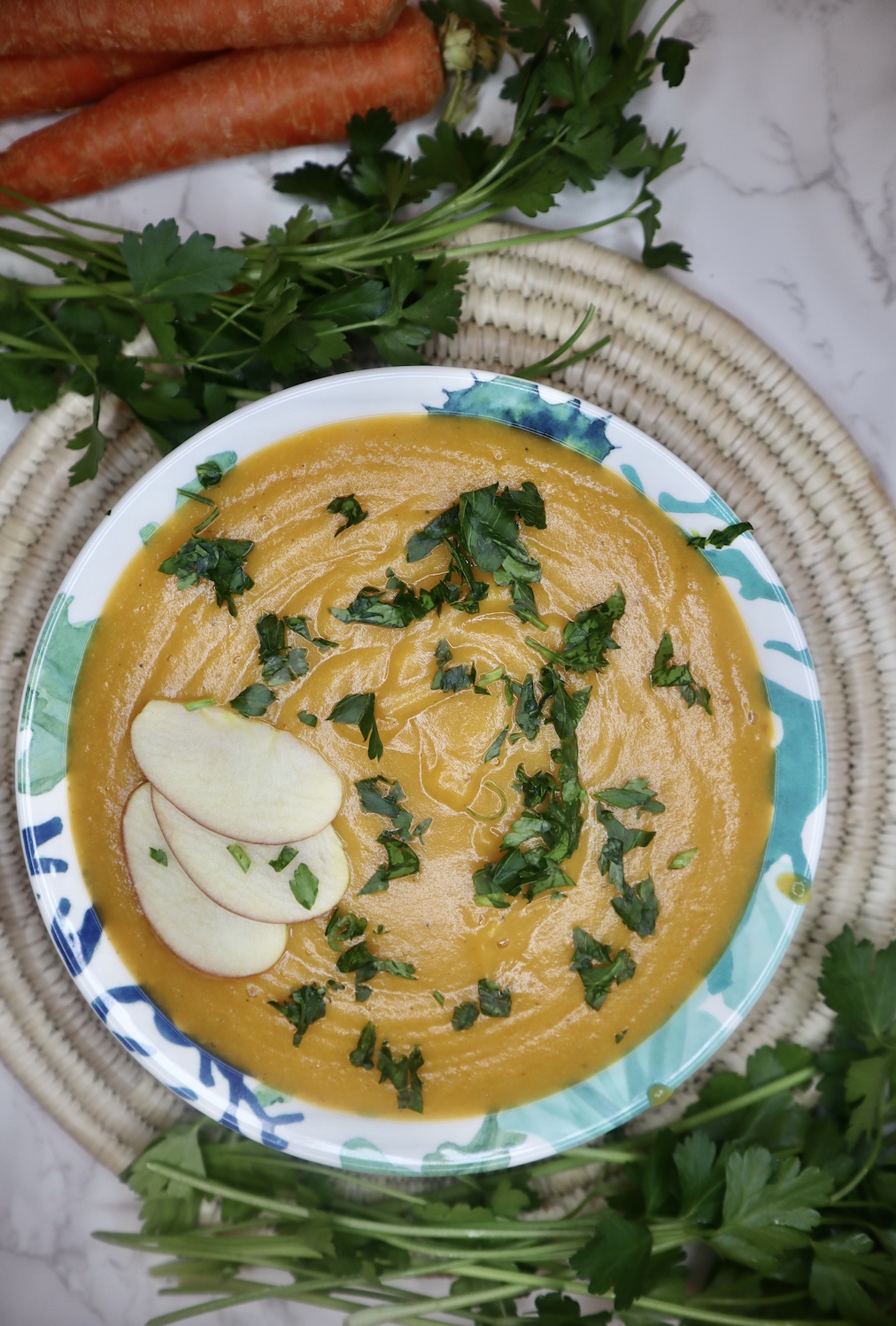 Carrot apple ginger soup next to carrots and parsley on a placemat