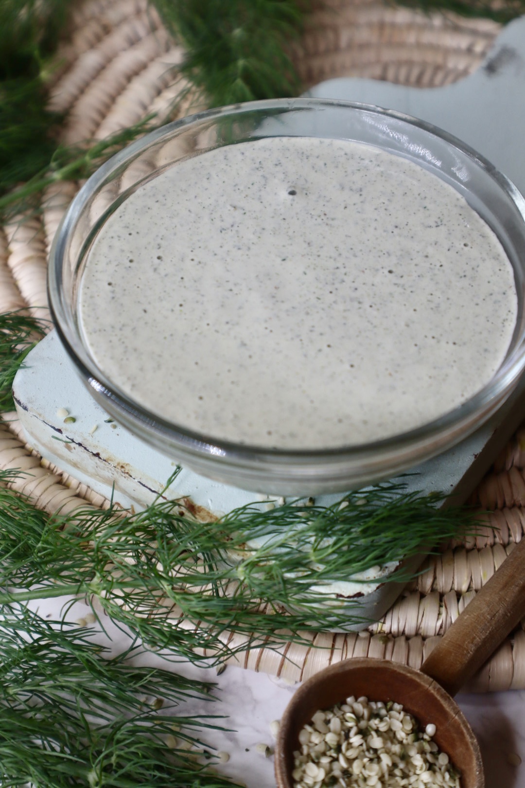 close up of hempseed ranch dressing next to fresh dill and a spoon of hemp seeds