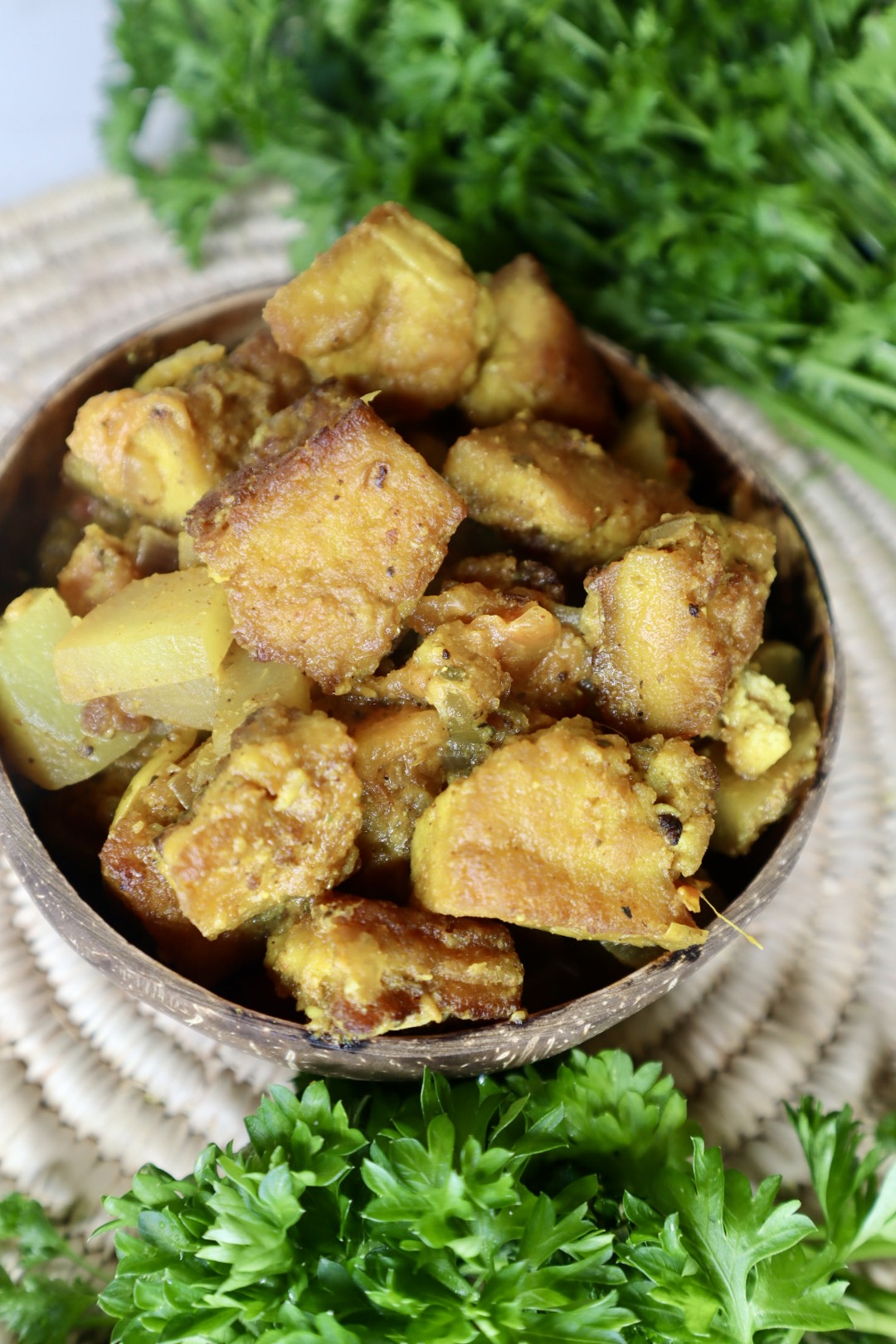 jamaican curry tofu in coconut bowl next to parsley greens