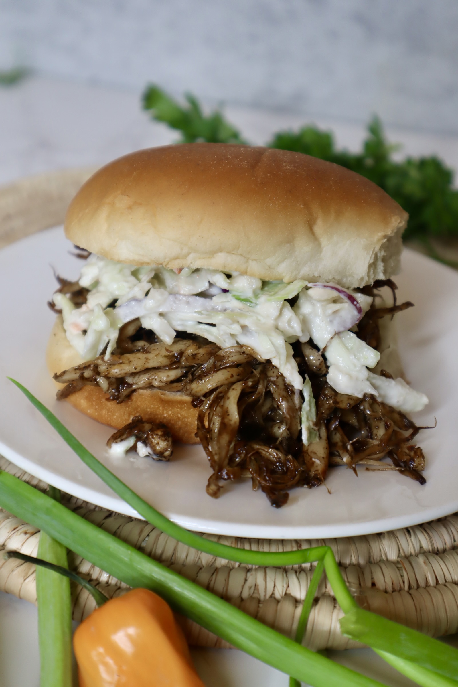 vegan jerk chicken sandwich on a white plate next to scallion