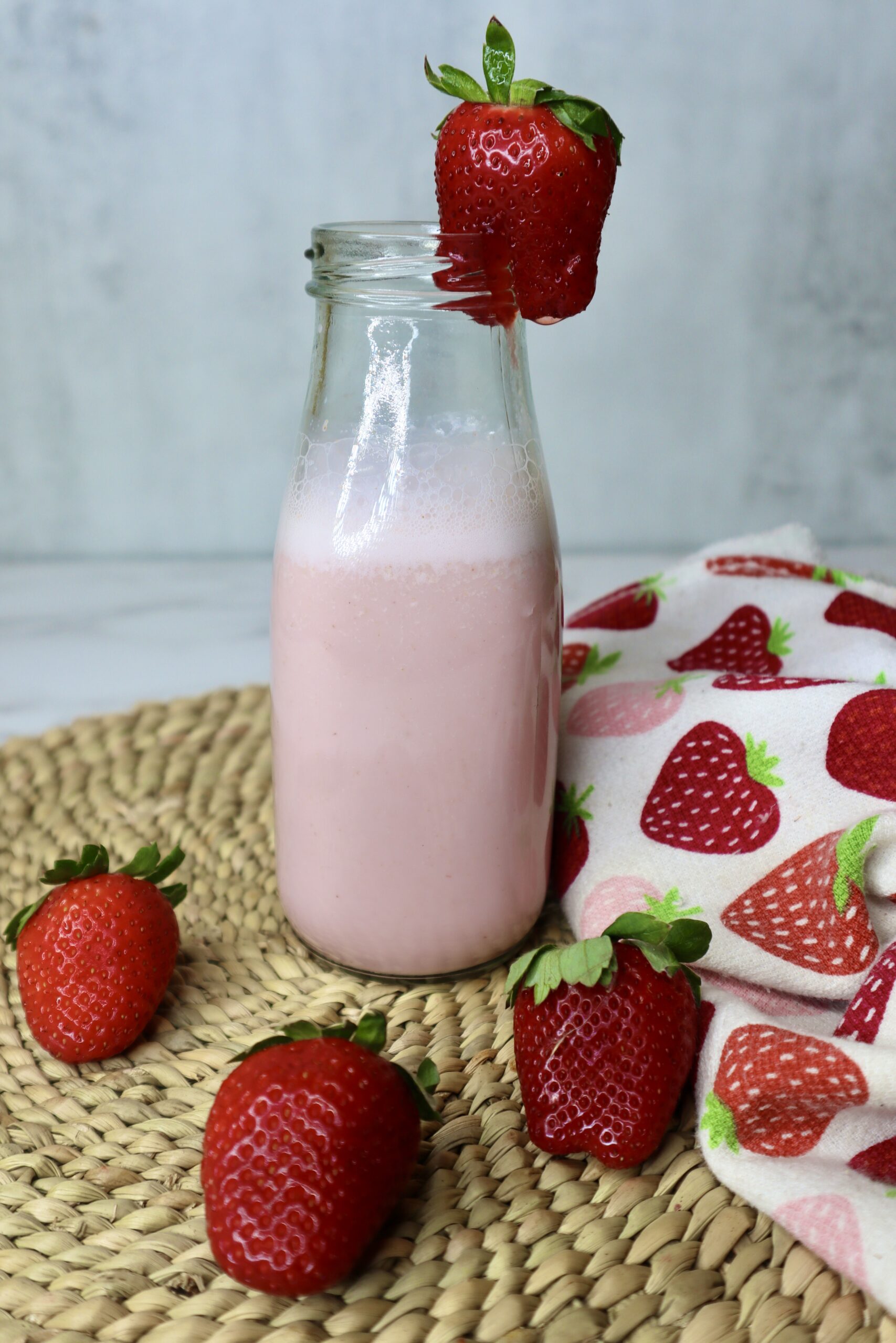 strawberry milk in a small milk glass next to fresh strawberries