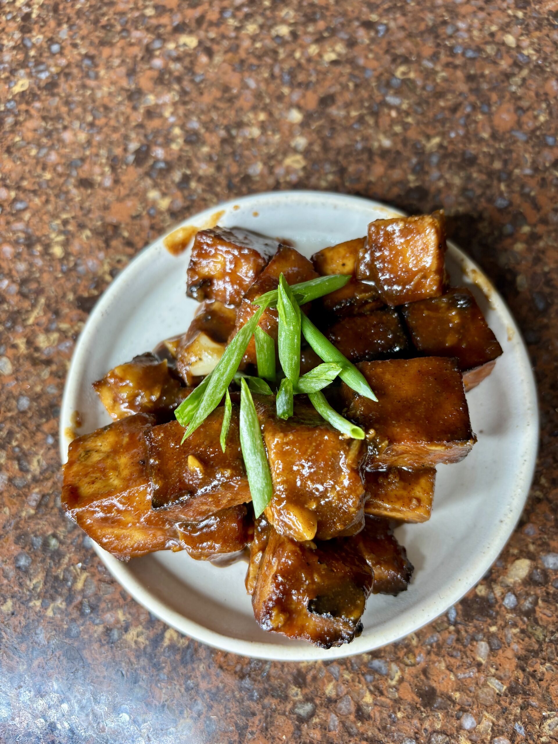 sweet glazed tofu covered in scallion on a white plate